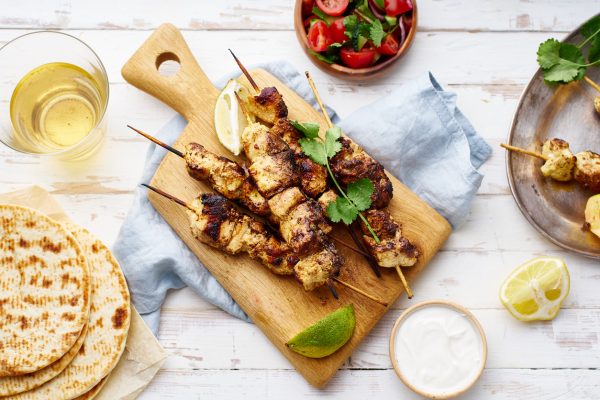 Chicken tikka kebab with red onion, coriander and fresh salad. Traditional indian dish made of chicken marinated in yoghurt and spices. Creative flatlay on white wooden background.