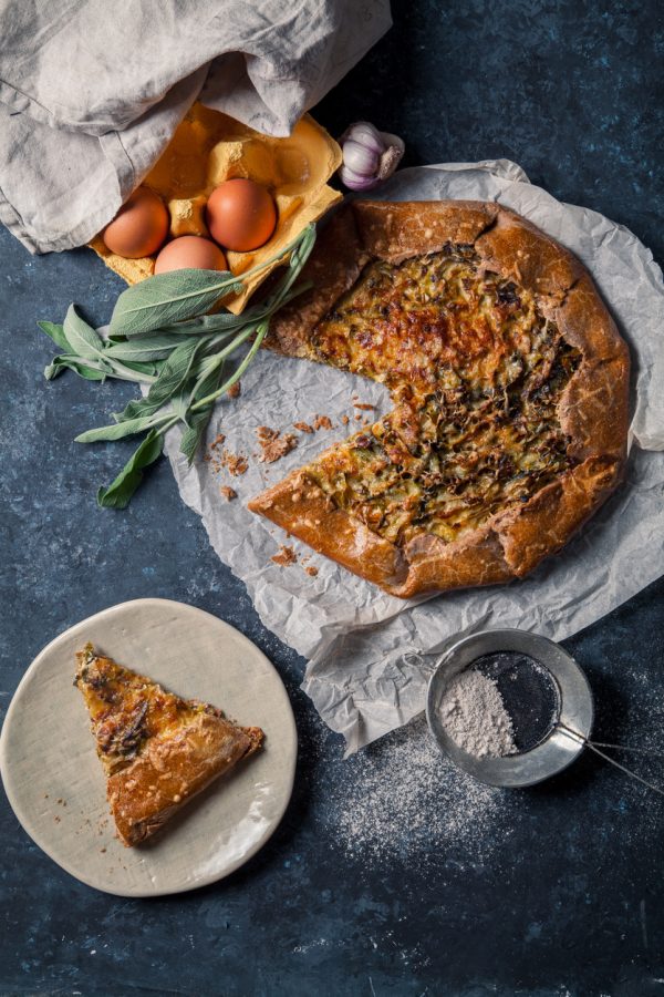 French styled leek and onion galette with sage and gruyere cheese made with wholegrain flour. Textured blue background. Rustic concept
