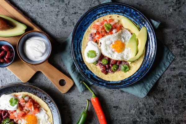 Huevos Rancheros Tostadas, Mexican breakfast consisting of toasted tortilla, chopped tomato and onion, jalapeno and beans, topped with fried egg, served with avocado slices and sour cream